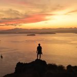 Silueta de una persona contemplando el atardecer sobre el mar desde un promontorio rocoso en Indonesia